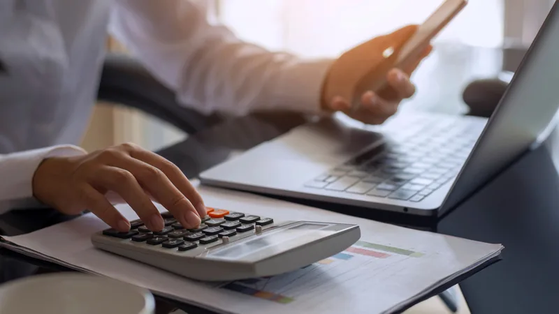 A person using a calculator beside a laptop